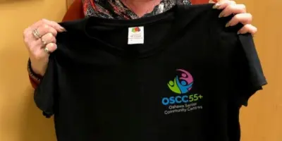 woman holding a black t-shirt with the OSCC55+ logo on it